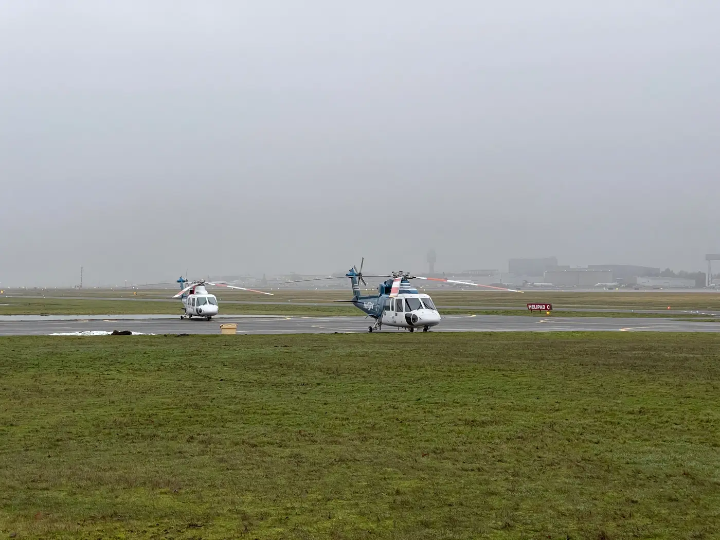 Two helicopters parked on a foggy airport apron with low visibility over the runway.